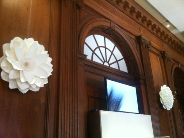 Two hanging, white flowers by Michele Tremblay sandwiching the animated architecture video. Photo by Gaby Heit