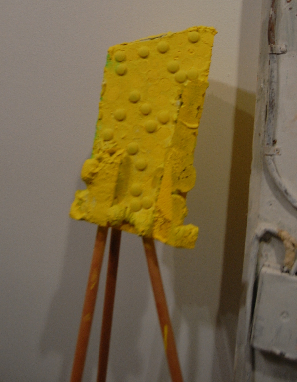 Something like a deformed, yellow Lego brick on an easel by Alexi Kukuljevic.