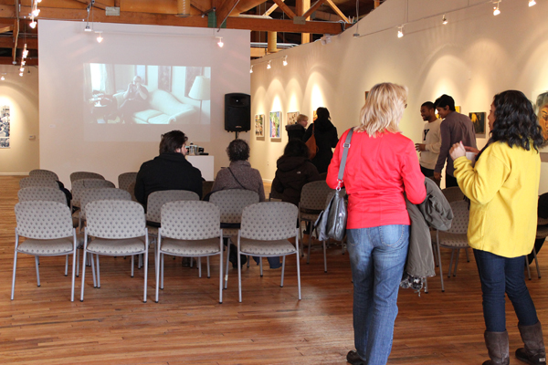 The crowd gathers for Saturday&squot;s Curator & Artist Talk; projected in the background, "Same Voices, Different Rooms," by Tommy Kha, a spliced reel of Phillip Seymour Hoffman in phone conversation with himself.