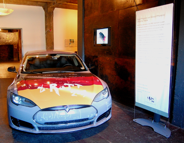 In the lobby, a Tesla car covered in "bad financial physics."