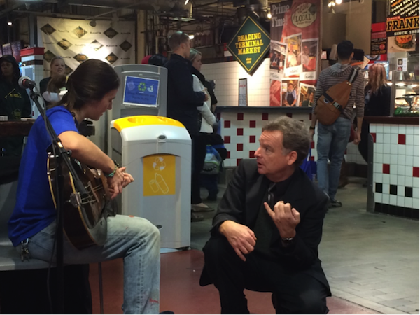 Paul Butler explains the four string tenor guitar to a Market patron