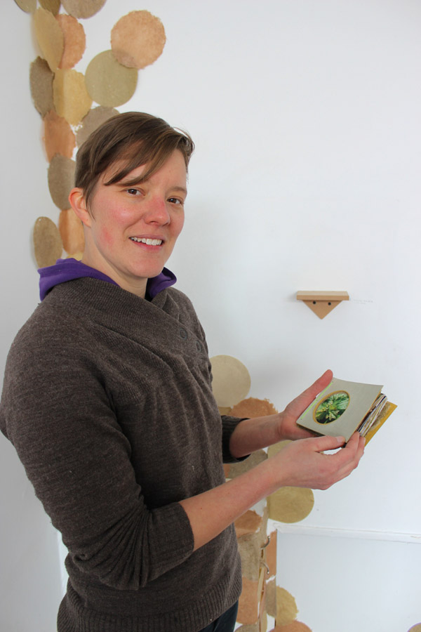Megan Heeres displays one of the books made from her paper. On the wall behind, you can see the growing installation of circles.
