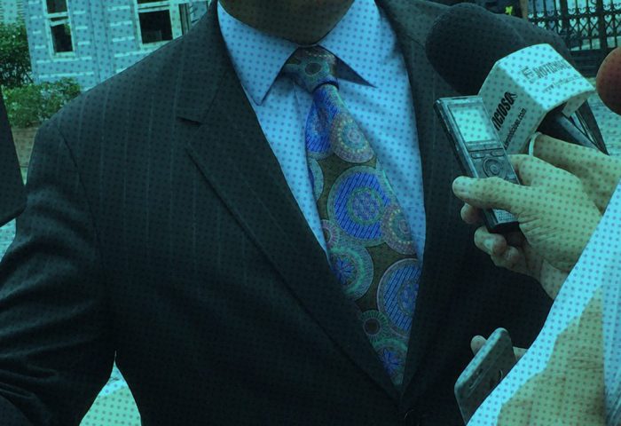 Reporters holding a camera, microphones, and a notebook surround an interviewee.